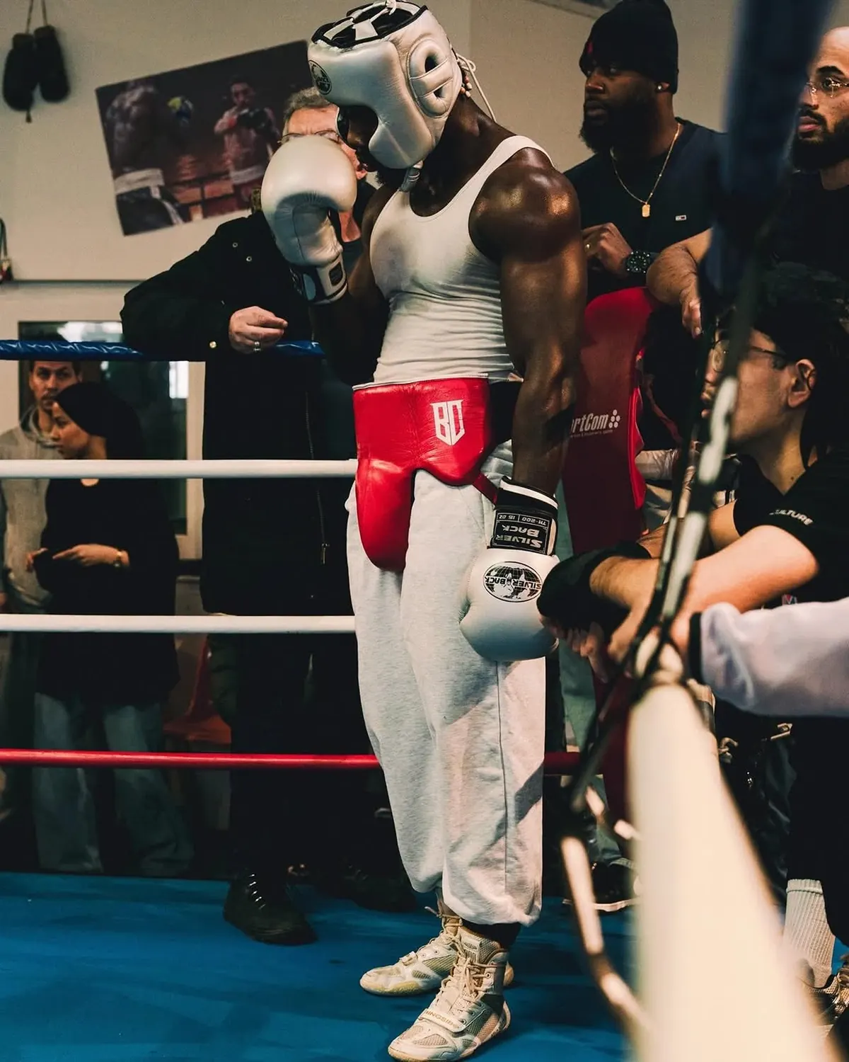 A boxer in headgear waiting in the corner of a ring before a round.